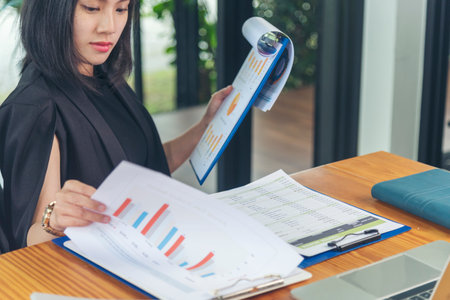 Asian Female freelance using laptop at home office desk. Woman reading financial graph chart Planning analyzing marketing data. Asian female people working office firm with business stuff, coffee cupの写真素材