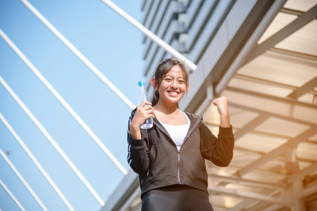 Women drinking water bottle running exercise in modern city wear wellness sportswear outside. Young woman workout outdoor exercising on bright sunny outside. Healthy wellness lifestyle woman conceptの写真素材