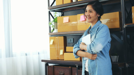 Asian woman startup small business at home office. Online seller entrepreneur young asian woman use tablet checking online order. Woman using tablet check stock goods supply delivery package shippingの写真素材