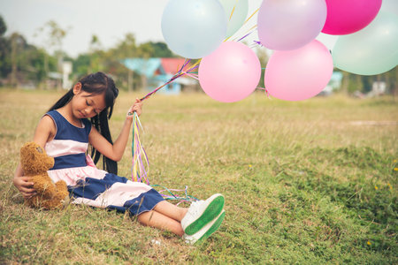 Happy Child hug teddy bear hold air balloon in green park playground. Teddy bear best friend for little kids cute girl. Autism happy playing together holding colorful helium balloons on playgroundの写真素材