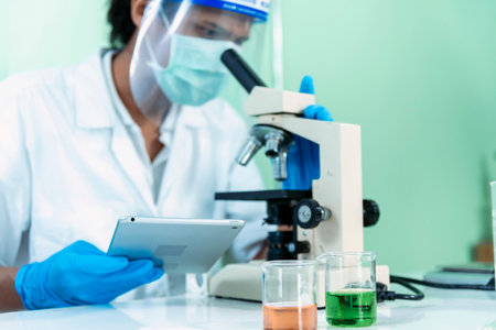Indian Scientist man look into Microscope research in science laboratory. Asian biochemistry scientist using microscope in laboratory chemistry labs. Covid-19 medical research scientific experimentの写真素材