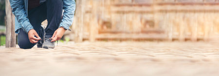 Banner Man kneels down rope tie shoes industry boots for worker. Close up shot of man hands tied shoestring for his brown construction boots. Close-up man hands tie up footwear shoes with copy spaceの写真素材
