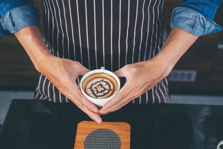 Close up hands of man sitting office desk holding sweet coffee cup relax and enjoy with happy time. Hot coffee mug in hand. Man holding coffee cup relaxing after work at office warm taste in cafeの写真素材