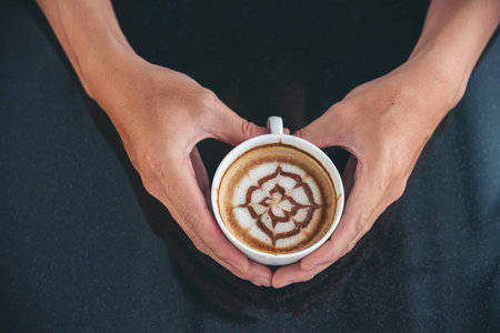 Close up hands of man sitting office desk holding sweet coffee cup relax and enjoy with happy time. Hot coffee mug in hand. Man holding coffee cup relaxing after work at office warm taste in cafeの写真素材
