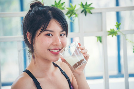 Asian women smile laugh look at camera health care home fitness lifestyle. Beautiful female drinking fresh milk low-fat dairy free lactose. Women hands holding white glass of milk pouring from bottleの写真素材