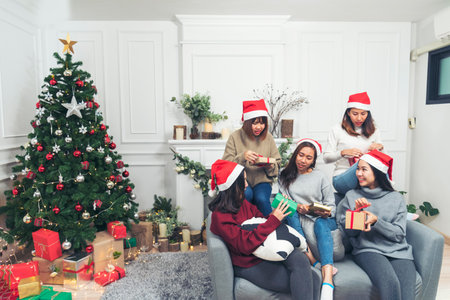 Group of Asian Woman party exchange christmas gift box under xmas tree surprise present gift. Young women holding gift box sitting living room celebrate christmas time xmas holiday winter festivalの写真素材