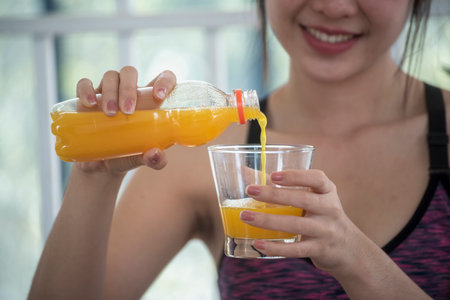 Women hands holding cold orange juice fresh fruit cool drinking. Asian women smile laugh look at camera health care home fitness lifestyle. Beautiful female pouring orange juice from cocktail bottleの写真素材