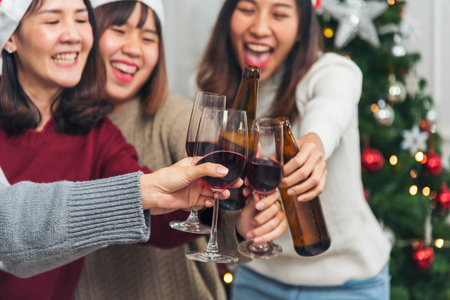 Christmas party Group of Asian Woman drink beer champagne exchange christmas gift box under xmas tree. Young women enjoy laughing sitting party together living room to celebrate Christmas holidayの写真素材