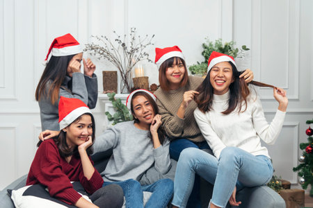 Christmas party Group of Asian Woman talk, play game, party, exchange christmas gift box under xmas tree. Young women enjoy laughing sitting together living room celebrate christmas holiday festivalの写真素材