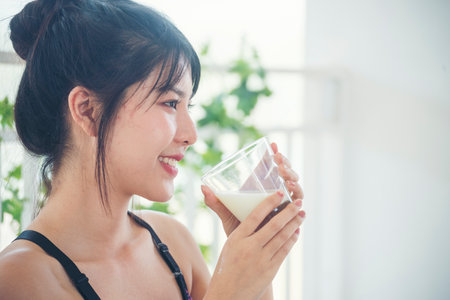 Asian women smile laugh look at camera health care home fitness lifestyle. Beautiful female drinking fresh milk low-fat dairy free lactose. Women hands holding white glass of milk pouring from bottleの写真素材