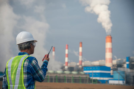 Senior Electrician engineer man hand holding red Walkie talkie communicate wear White hardhat at Power stations manufacturing electrical plant. Technician worker blue hard hat helmet Engineer industryの写真素材