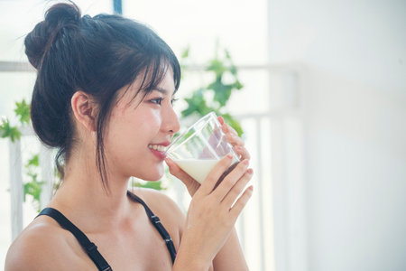 Women hands holding white glass of milk pouring from bottle. Asian women smile laugh look at camera health care home fitness lifestyle. Beautiful female drinking fresh milk low-fat dairy free lactoseの写真素材