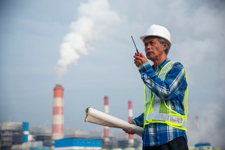 Senior Electrician engineer man hand holding red Walkie talkie communicate wear White hardhat at Power stations manufacturing electrical plant. Technician worker blue hard hat helmet Engineer industryの写真素材