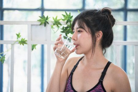 Woman drinking water hands holding cold mineral water cool drinking. Asian women smile laugh look away health care home fitness lifestyle. Cheerful Beautiful female drink glass of water smile faceの写真素材