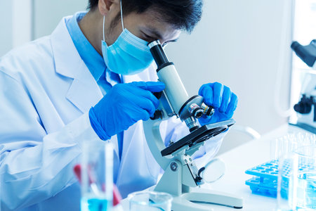 Scientist man look into Microscope research in science laboratory. Asian scientist look at microbiology microscope laboratory equipment chemistry lab. Biochemistry research experiment vaccine conceptの写真素材