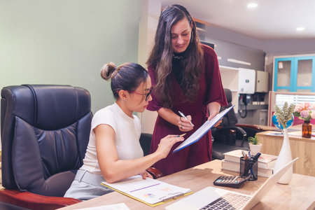 Diversity Two Businesswoman working together in office desk. Two cuacasian asian women look at financial report document as partner teamwork. Team leader coworker brainstorming executive entrepreneurの写真素材