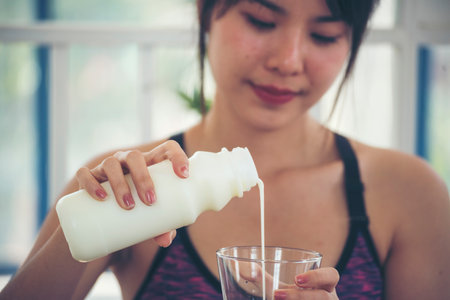 Asian women smile laugh look at camera health care home fitness lifestyle. Beautiful female drinking fresh milk low-fat dairy free lactose. Women hands holding white glass of milk pouring from bottleの写真素材