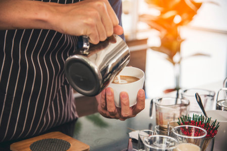 Coffee barista pour espresso shot and make latte art hot coffee cup. Cappuccino with milk in italian coffee shop cafe. Close up hands of barista make brown latte art for customer cafeteria.の写真素材