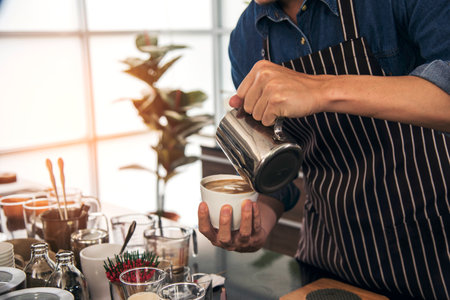 Coffee barista pour espresso shot and make latte art hot coffee cup. Cappuccino with milk in italian coffee shop cafe. Close up hands of barista make brown latte art for customer cafeteria.の写真素材