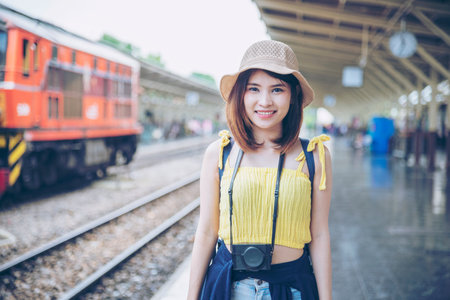 Portrait young asian traveller woman smiling sitting railway station look at camera. Beautiful women tourist relaxing using camera hold on digital tablet while waiting train departure enjoy holidayの写真素材