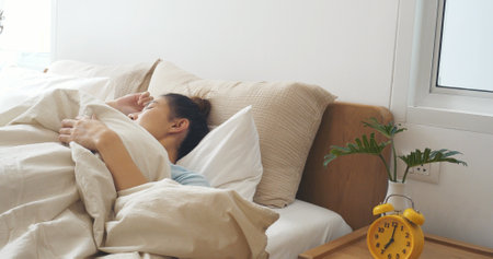 Asian women sleep wake up in white cozy bedroom happy time morning sunrise. Beautiful chinese use hand stop time alarm clock. Happy person lifestyle wake up in morning wellbeing relax sleepy nappingの写真素材