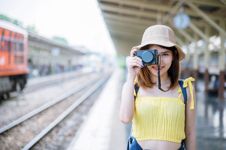Portrait young asian traveller woman smiling sitting railway station look at camera. Beautiful women tourist relaxing using camera hold on digital tablet while waiting train departure enjoy holidayの写真素材