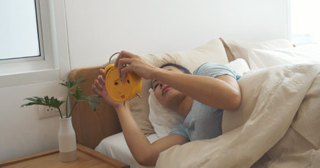 Asian women sleep wake up in white cozy bedroom happy time morning sunrise. Beautiful chinese use hand stop time alarm clock. Happy person lifestyle wake up in morning wellbeing relax sleepy nappingの写真素材