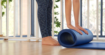 Woman hands rolled up yoga mat on gym floor in yoga fitness training room. Home workout woman close up hands rolling foam yoga gym mat. Woman barefoot home workout sportive healthy lifestyle conceptの写真素材