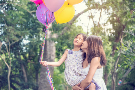 Happiness mother daughter play balloons together in green garden park outdoor lifestyle. Happy family two people enjoy have fun cheerful smile. Mother childhood hand holding colorful balloons outsideの写真素材