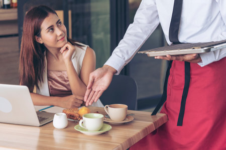 Restaurant business Handsome waiter serving food to young beautiful women with smiling face. Businesswoman using computer laptop while working on luch time. Waiter Man serving coffee cup in cafeの写真素材