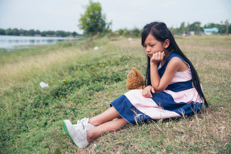 Sad girl hugging teddy bear sadness alone in green garden park. Lonely girl feeling sad unhappy sitting outdoors with best friend toy. Autism child play teddy bear best friend.の写真素材