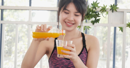 Asian women smile laugh look at camera health care home fitness lifestyle. Women hands holding cold orange juice fresh fruit cool drinking. Beautiful female pouring orange juice from cocktail bottleの写真素材
