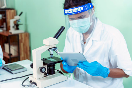 Indian Scientist man look into Microscope research in science laboratory. Asian biochemistry scientist using microscope in laboratory chemistry labs. Covid-19 medical research scientific experimentの写真素材