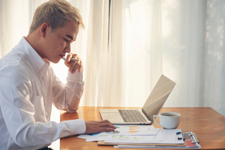 Portrait Asian Businessman typing laptop computer drinking coffee cup at office desk via wireless internet technology working online. Asian handsome man Freelance business person confident managerの写真素材