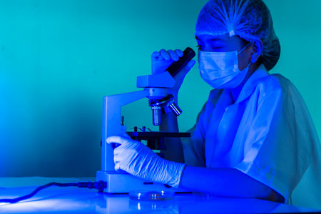 Woman scientist in lab look at science microscope medical test researching biology chemistry in blue...