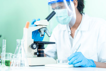 Scientist man look into Microscope research in science laboratory. Asian scientist looking equipment laboratory chemistry labs. Covid-19 coronavirus biochemistry research experiment vaccine conceptの写真素材