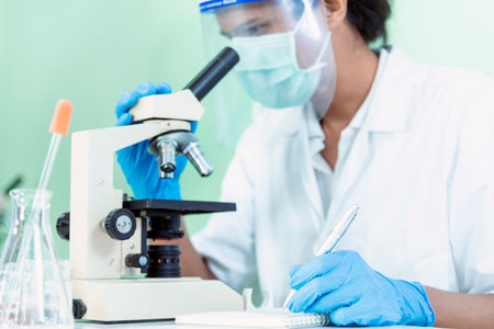 Indian Scientist man look into Microscope research in science laboratory. Asian biochemistry scientist using microscope in laboratory chemistry labs. Covid-19 medical research scientific experimentの写真素材