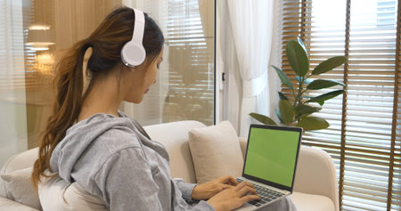 Happy asian woman use headphones listen to music online web conference sitting on cozy sofa in living room at home. Female asian people working at home research watching online e-learning video callの写真素材