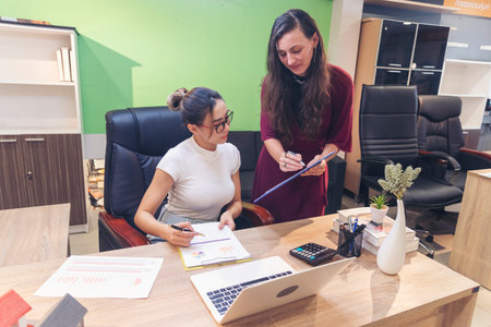 Diversity Two Businesswoman working together in office desk. Two cuacasian asian women look at financial report document as partner teamwork. Team leader coworker brainstorming executive entrepreneurの写真素材