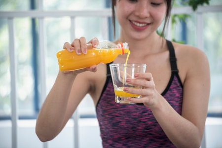 Asian women smile laugh look at camera health care home fitness lifestyle. Women hands holding cold orange juice fresh fruit cool drinking. Beautiful female pouring orange juice from cocktail bottleの写真素材