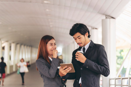 Young Asian Business people smiling Relax holding a cup of coffee before go to work. Couple lover enjoy drinking coffee together in modern city. Business people holding cup of coffee at officeの写真素材