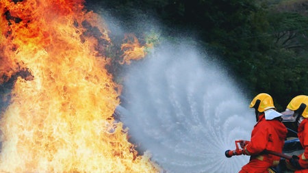 Firefighter Rescue team training in fire fighting extinguisher. Teamwork Firefighter fighting with flame using fire hose chemical water foam spray engine. Fireman teams wear hard hat safety uniformの写真素材