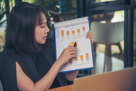 Business woman using smartphone, laptop on office desk. Female freelance reading financial graph charts Planning analyzing marketing data. Hands of young woman working in office firm business info.の写真素材