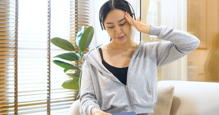 asian woman use headphones listen to music reading book sitting on cozy sofa in living room at home....