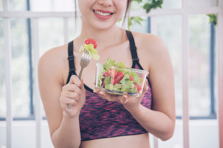 Wellness Asian women dressing organic green salad tomato vegetable dish. Beautiful girl healthcare vegan wellness lifestyle concept. Healthy woman workout holding organic salad bowl healthy lifestyleの写真素材