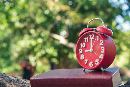 Alarm clock Red vintage retro time on book and tree green nature bokeh nature deadline concept.