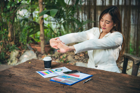 Woman streching arm raised sitting incorrect position home office desk. Back side of young asian woman tired from work body stress back pain office syndrome. Female work from home new normal conceptの写真素材