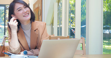 Happy asian woman video call web conference sitting on cozy sofa in living room at home. Smile Female asian people use laptop notebook computer headphones online call working from home watching videoの写真素材