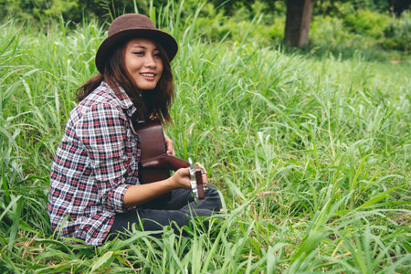 Young women playing acoustic guitar outdoor in green park. Woman person playing acoustic guitar...