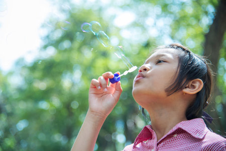 Adorable happy cute girl playful foam bubbles in green playground in summer outdoors. Funny Cheerful...
